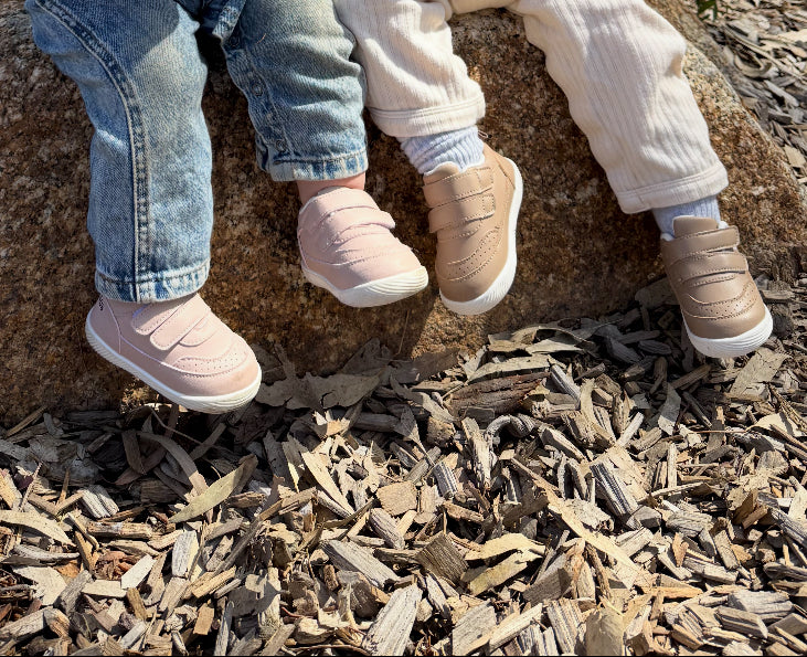 Two pairs of feet wearing shoes on a ground covered with wood chips.